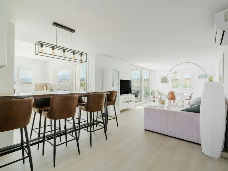 Salón y cocina abierta luminosos, con muebles despejados y luz natural entrando por un ventanal